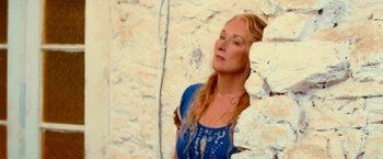 Movie still from “Mamma Mia!” (2008), directed by Phyllida Lloyd – A woman standing next to a stone wall; Close Up shot, Low angle