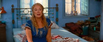 Movie still from “Mamma Mia!” (2008), directed by Phyllida Lloyd – A woman sitting in front of a bed in a room; Medium shot, Over the shoulder angle