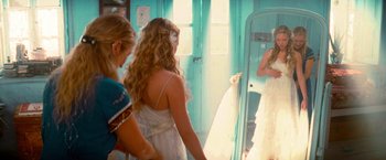 Movie still from “Mamma Mia!” (2008), directed by Phyllida Lloyd – Two women looking in a mirror while one of them is holding onto a dress; Medium shot, Over the shoulder angle