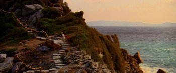 Movie still from “Mamma Mia!” (2008), directed by Phyllida Lloyd – A person walking down a stone path on a cliff; Extreme Wide shot, High angle