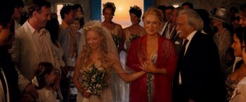Movie still from “Mamma Mia!” (2008), directed by Phyllida Lloyd – Two women in wedding dresses standing next to each other in front of a group of people; Medium shot, High angle