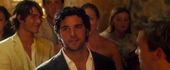 Movie still from “Mamma Mia!” (2008), directed by Phyllida Lloyd – A group of people standing in a room with a man in a suit; Close Up shot, Over the shoulder angle