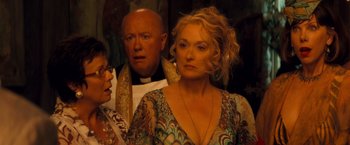 Movie still from “Mamma Mia!” (2008), directed by Phyllida Lloyd – A man and a woman standing next to each other in front of a priest; Close Up shot, Over the shoulder angle