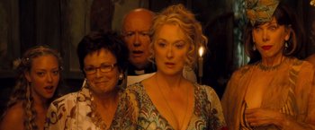 Movie still from “Mamma Mia!” (2008), directed by Phyllida Lloyd – A man and a woman standing next to each other in front of a priest; Close Up shot, Over the shoulder angle