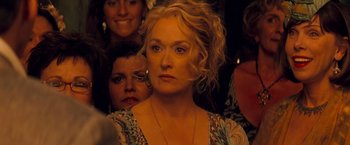 Movie still from “Mamma Mia!” (2008), directed by Phyllida Lloyd – A person with a crowd in the background; Close Up shot, Over the shoulder angle