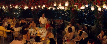 Movie still from “Mamma Mia!” (2008), directed by Phyllida Lloyd – A group of people sitting around a table with food; Wide shot, High angle