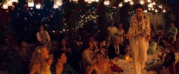Movie still from “Mamma Mia!” (2008), directed by Phyllida Lloyd – A group of people sitting around a table at a party; Wide shot, Over the shoulder angle