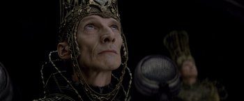 Movie still from “Man of Steel” (2013), directed by Zack Snyder – An old man wearing a crown and a microphone in the background; Close Up shot, Overhead angle