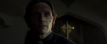 Movie still from “Man of Steel” (2013), directed by Zack Snyder – A man in a priest's outfit in front of a cross; Close Up shot, Low angle