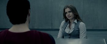 Movie still from “Man of Steel” (2013), directed by Zack Snyder – A woman sitting at a table in front of a wall; Medium shot, Over the shoulder angle