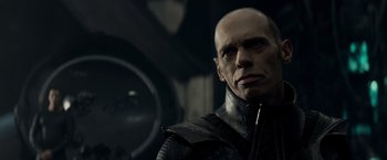 Movie still from “Man of Steel” (2013), directed by Zack Snyder – A bald man in a black jacket looking at the camera; Close Up shot, Over the shoulder angle