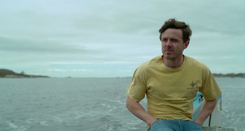 Movie still from “Manchester by the Sea” (2016), directed by Kenneth Lonergan – A man in a yellow shirt standing in front of a body of water; Medium shot, Low angle