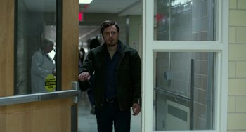 Movie still from “Manchester by the Sea” (2016), directed by Kenneth Lonergan – A man walking through a hallway in front of a door; Medium shot, Over the shoulder angle
