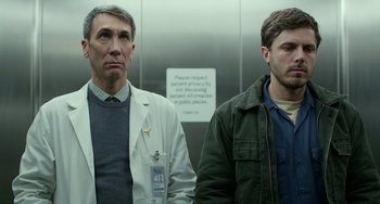 Movie still from “Manchester by the Sea” (2016), directed by Kenneth Lonergan – Two men standing next to each other in front of an elevator; Medium shot, Low angle