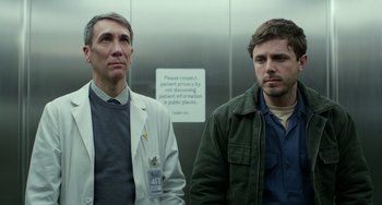 Movie still from “Manchester by the Sea” (2016), directed by Kenneth Lonergan – Two men standing next to each other in front of an elevator; Medium shot, Low angle