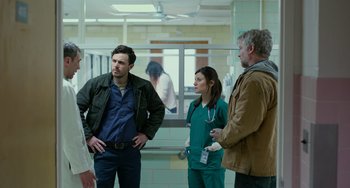 Movie still from “Manchester by the Sea” (2016), directed by Kenneth Lonergan – A group of people standing around in a room; Medium shot, Over the shoulder angle