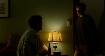 Movie still from “Manchester by the Sea” (2016), directed by Kenneth Lonergan – Two young men standing in front of a table with a lamp on it; Medium shot, Over the shoulder angle