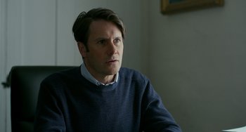 Movie still from “Manchester by the Sea” (2016), directed by Kenneth Lonergan – A man sitting in front of a wall looking at the camera; Close Up shot, Over the shoulder angle
