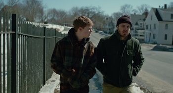 Movie still from “Manchester by the Sea” (2016), directed by Kenneth Lonergan – Two young men walking down a sidewalk near a fence; Medium shot, Over the shoulder angle
