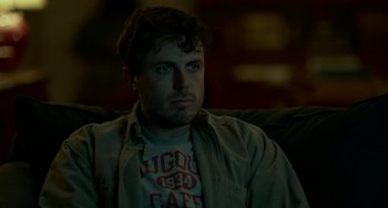 Movie still from “Manchester by the Sea” (2016), directed by Kenneth Lonergan – A man sitting on a couch in the dark; Close Up shot, Over the shoulder angle
