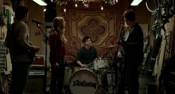 Movie still from “Manchester by the Sea” (2016), directed by Kenneth Lonergan – A group of people that are sitting around a drum set; Wide shot, Over the shoulder angle