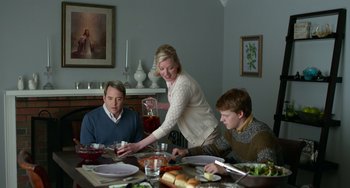 Movie still from “Manchester by the Sea” (2016), directed by Kenneth Lonergan – A woman standing at a dinner table with two men; Medium shot, Over the shoulder angle