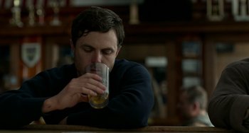 Movie still from “Manchester by the Sea” (2016), directed by Kenneth Lonergan – A man is drinking a glass of beer at a bar; Close Up shot, Over the shoulder angle