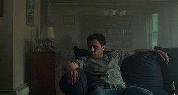 Movie still from “Manchester by the Sea” (2016), directed by Kenneth Lonergan – A man sitting on a couch in a living room; Medium shot, High angle