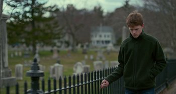 Movie still from “Manchester by the Sea” (2016), directed by Kenneth Lonergan – A young man standing in front of a fence in front of a cemetery; Medium shot, Over the shoulder angle