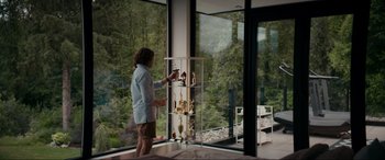 Movie still from “Margaux” (2022), directed by Steven C. Miller – A woman standing in front of a large window looking outside; Medium shot, Low angle