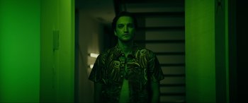 Movie still from “Margaux” (2022), directed by Steven C. Miller – A man standing in the dark wearing a green shirt; Medium shot, Low angle
