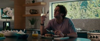 Movie still from “Margaux” (2022), directed by Steven C. Miller – A man sitting at a table with a fork in his mouth; Medium shot, Low angle