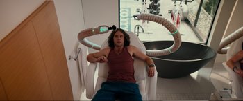 Movie still from “Margaux” (2022), directed by Steven C. Miller – A man sitting in a white chair with a machine on his head; Medium shot, Over the shoulder angle