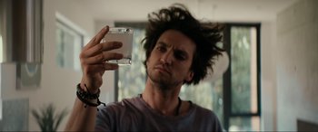 Movie still from “Margaux” (2022), directed by Steven C. Miller – A man holding up a compact disc in front of his face; Close Up shot, Low angle