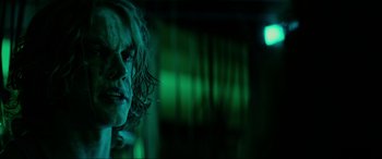 Movie still from “Margaux” (2022), directed by Steven C. Miller – A woman with long hair is standing in the dark; Close Up shot, Over the shoulder angle