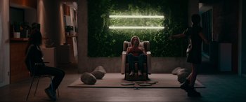 Movie still from “Margaux” (2022), directed by Steven C. Miller – A person sitting in a chair in a room; Wide shot, Low angle