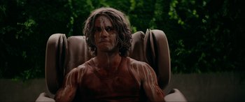 Movie still from “Margaux” (2022), directed by Steven C. Miller – A man sitting in a chair with brown hair and a red shirt; Close Up shot, High angle