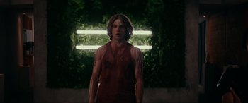 Movie still from “Margaux” (2022), directed by Steven C. Miller – A man with long hair is standing in front of a wall; Medium shot, Low angle