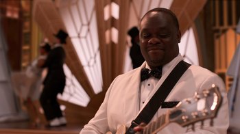 A man in a white suit and bow tie playing an electric guitar