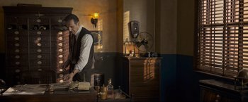 Movie still from “Marlowe” (2022), directed by Neil Jordan – A man standing at a desk in front of a window; Medium shot, Low angle