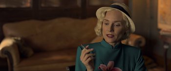 Movie still from “Marlowe” (2022), directed by Neil Jordan – A woman in a hat smoking a cigarette in a chair; Close Up shot, Over the shoulder angle