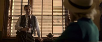 Movie still from “Marlowe” (2022), directed by Neil Jordan – A man standing in front of a window talking to another man; Medium shot, Over the shoulder angle