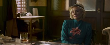 Movie still from “Marlowe” (2022), directed by Neil Jordan – A woman sitting in front of a table in a room; Medium shot, Over the shoulder angle