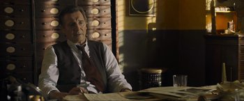 Movie still from “Marlowe” (2022), directed by Neil Jordan – An older man sitting at a table in front of papers; Medium shot, Low angle