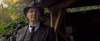 Movie still from “Marlowe” (2022), directed by Neil Jordan – An older man wearing a suit and a hat; Close Up shot, Over the shoulder angle