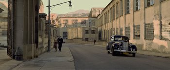 Movie still from “Marlowe” (2022), directed by Neil Jordan – A man walking down a street with a car; Extreme Wide shot, High angle