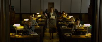 Movie still from “Marlowe” (2022), directed by Neil Jordan – A woman standing in front of a group of people in a room; Wide shot, Low angle