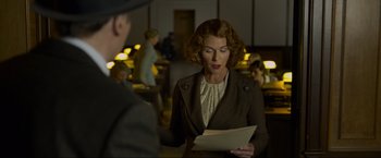 Movie still from “Marlowe” (2022), directed by Neil Jordan – A woman in a brown jacket is reading a piece of paper; Medium shot, Over the shoulder angle