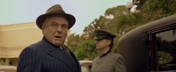 Movie still from “Marlowe” (2022), directed by Neil Jordan – A man wearing a hat and glasses standing next to another man wearing a hat and glasses; Close Up shot, Over the shoulder angle