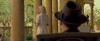 Movie still from “Marlowe” (2022), directed by Neil Jordan – A woman in a white dress standing next to a man in a hat; Medium shot, Over the shoulder angle